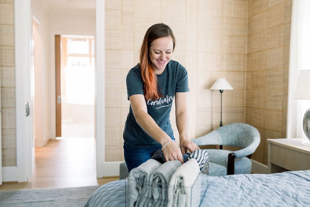 Woman in a bedroom folding clothes and putting them in a clear container.